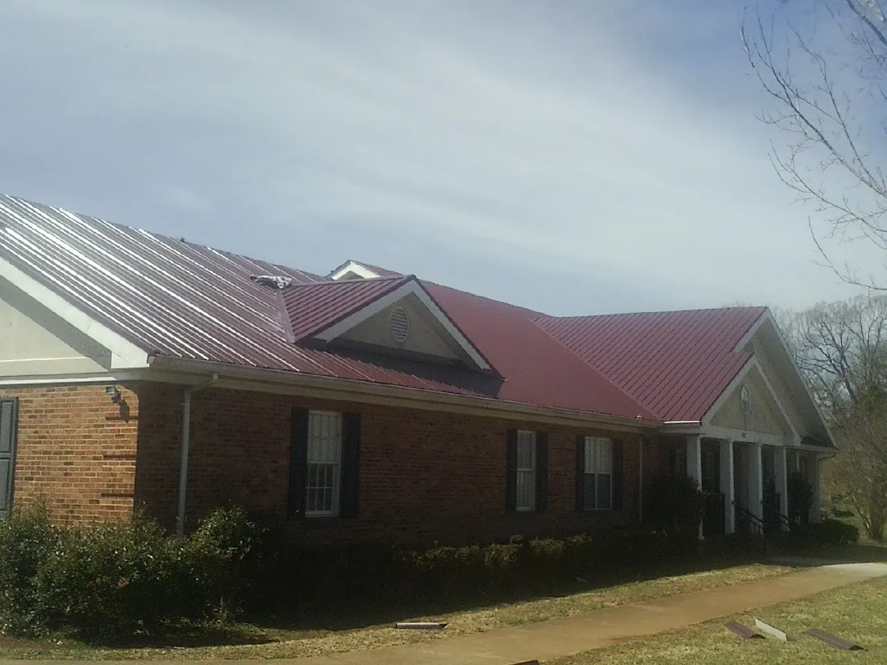 Red metal roof with gabled entries on a long brick building, from a Hail Damage Roof Repair job in Shepherd